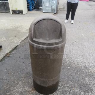Heavy-duty round trash can with flip lid, used condition, outdoor setting. Durable construction for high-traffic areas.