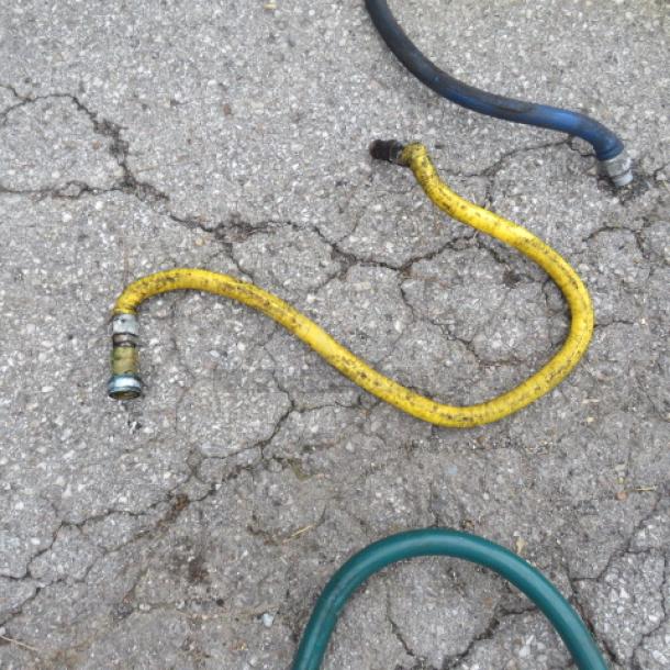 Yellow gas line hose on concrete, worn condition. Ends have metal fittings for connection. Suitable for gas appliances.