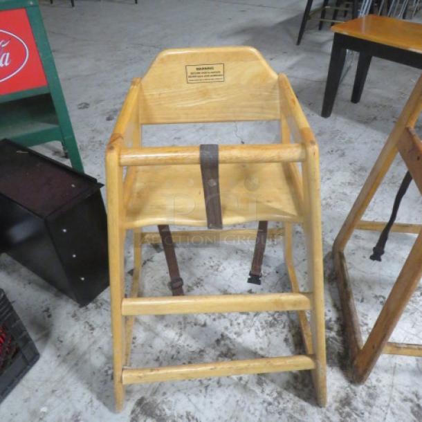 Wooden high chair with safety straps, natural finish, used condition. Features safety warning label. Ideal for dining use.
