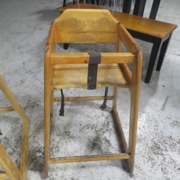 Wooden high chair with safety straps, shows wear; suitable for vintage decor or functional use.
