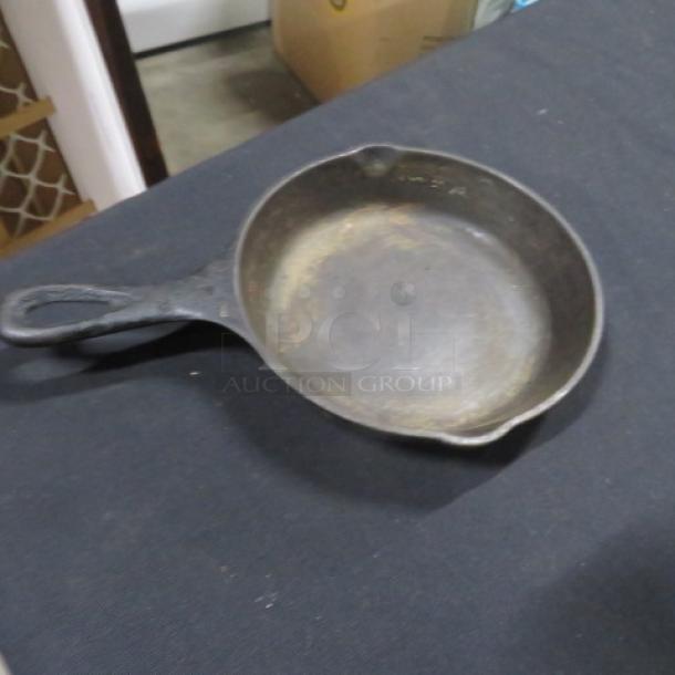 Lodge 6.5-inch cast iron skillet with visible wear; seasoned surface, ergonomic handle, dual pour spouts.