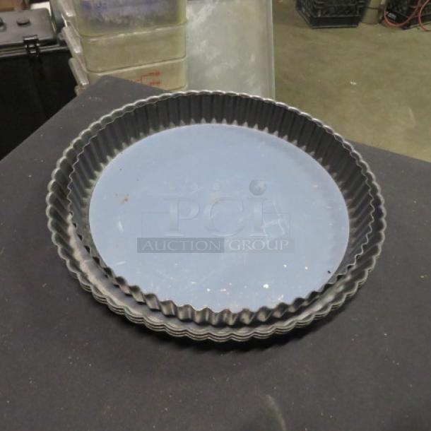 Assorted bake pans, metal, fluted edges, stacked on black surface, some wear visible. Ideal for baking pies or tarts.