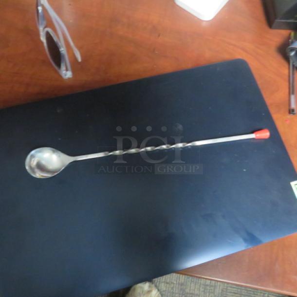 New Swizzel spoon with twisted handle and red tip, lying on a black surface. Ideal for stirring drinks.