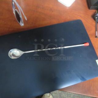 New Swizzel spoon with twisted handle and red tip, lying on a black surface. Ideal for stirring drinks.