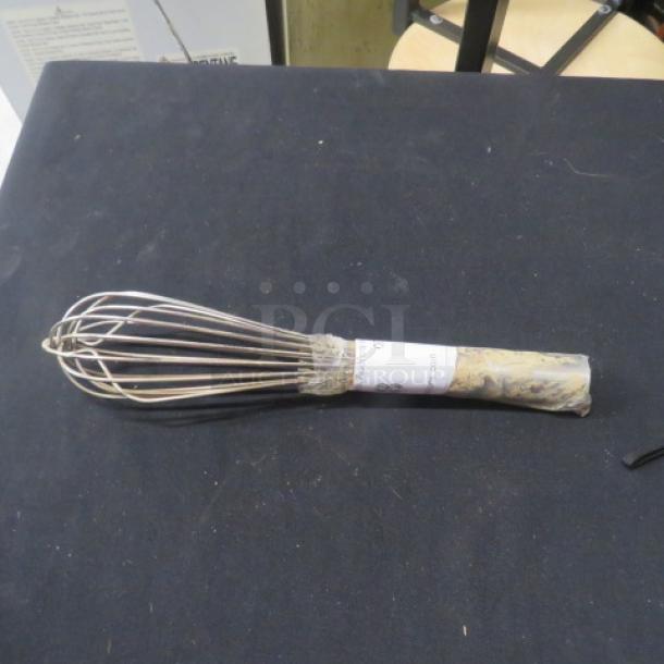 Stainless steel whip with wire loops, partially wrapped handle, and visible label. In used condition on black surface.