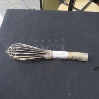 Stainless steel whip with wire loops, partially wrapped handle, and visible label. In used condition on black surface.