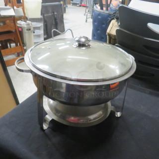 Stainless steel round chafer with glass lid, dual handles. Features elevated stand, excellent condition for catering use.