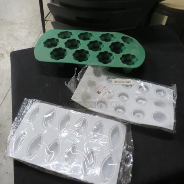 Assorted silicone baking molds, including green floral and two white designs, in new condition with packaging.