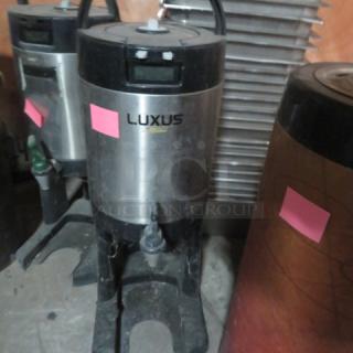 Fetco Luxus 1.5 gallon beverage dispenser on stand, model L3D-15. Features stainless steel body, visible spout, and handle.