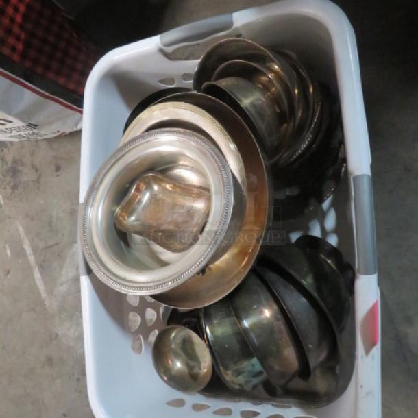 Assorted silver-plated serveware in a basket, including trays and bowls. Items exhibit tarnishing, indicating vintage condition.