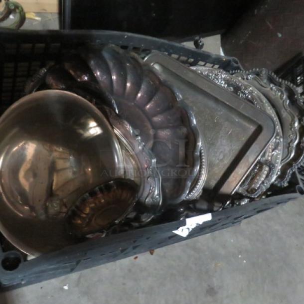 Assorted silver-plated serveware lot with various trays and bowls, featuring ornate designs and tarnished patina, in storage bin.