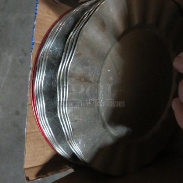 Assorted charger plates, stacked, featuring metallic finish with fluted edges, displayed in a cardboard box. Condition appears used.
