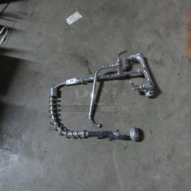 Commercial dish faucet with sprayer, chrome finish, flexible spring hose, and dual handles. Moderate wear visible.