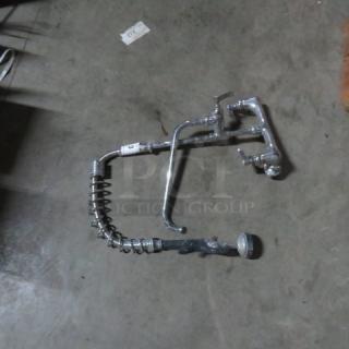 Commercial dish faucet with sprayer, chrome finish, flexible spring hose, and dual handles. Moderate wear visible.