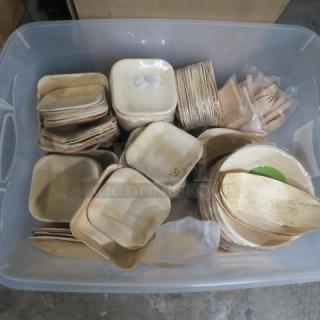 Plastic container filled with assorted bamboo plates, bowls, and utensils in various shapes and sizes, new condition.