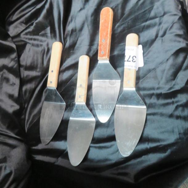 Four metal pizza/pie servers with wooden handles on black fabric. One server has a "371" tag attached.