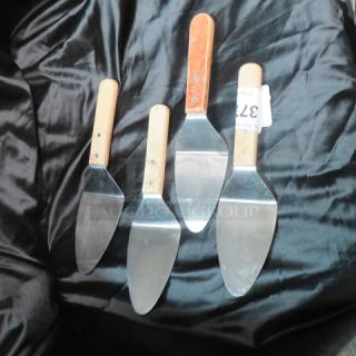 Four metal pizza/pie servers with wooden handles on black fabric. One server has a "371" tag attached.