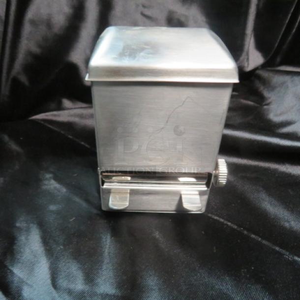 Stainless steel toothpick dispenser, new condition, sleek design with manual control knob, on black background.