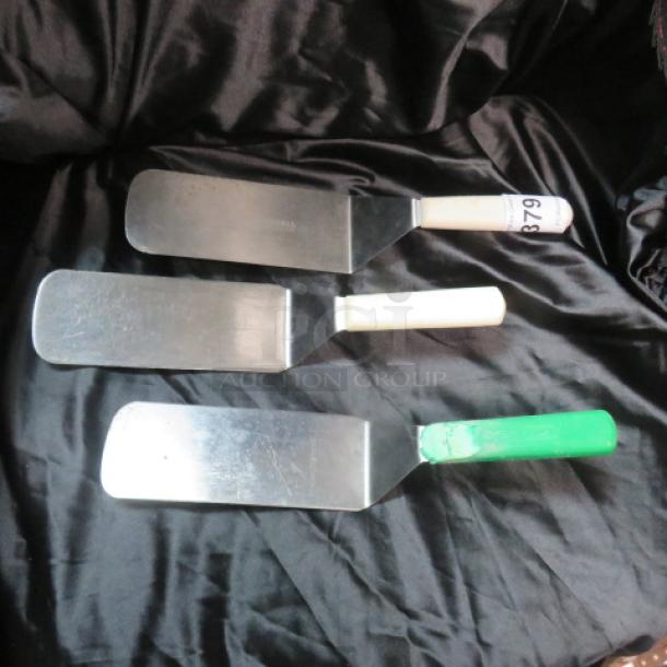 Three stainless steel hamburger turners with different colored handles, one labeled "879," in good condition.