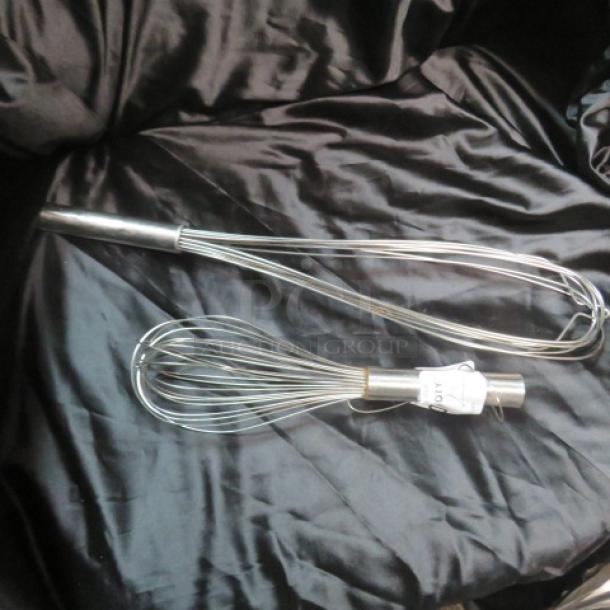 Two assorted stainless steel whisks, different sizes, on a black fabric background; tags attached.