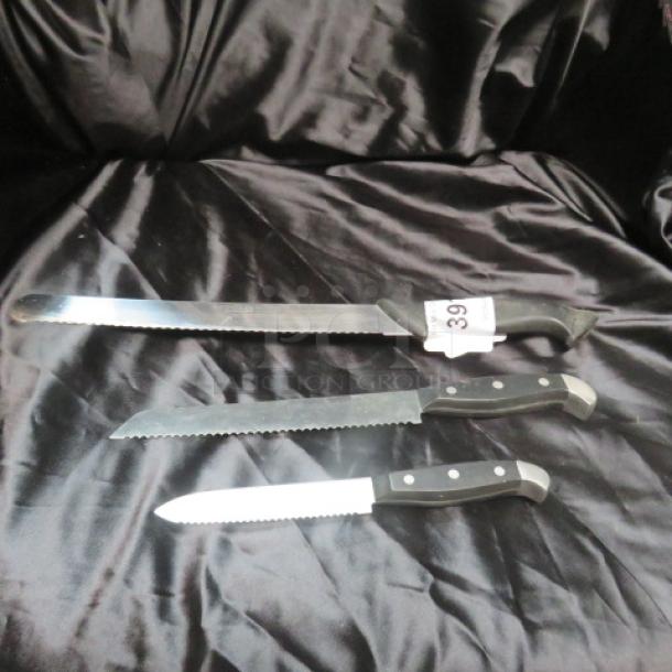 Assorted chef knives on black fabric; includes three serrated blades with black handles. One knife labeled "39."