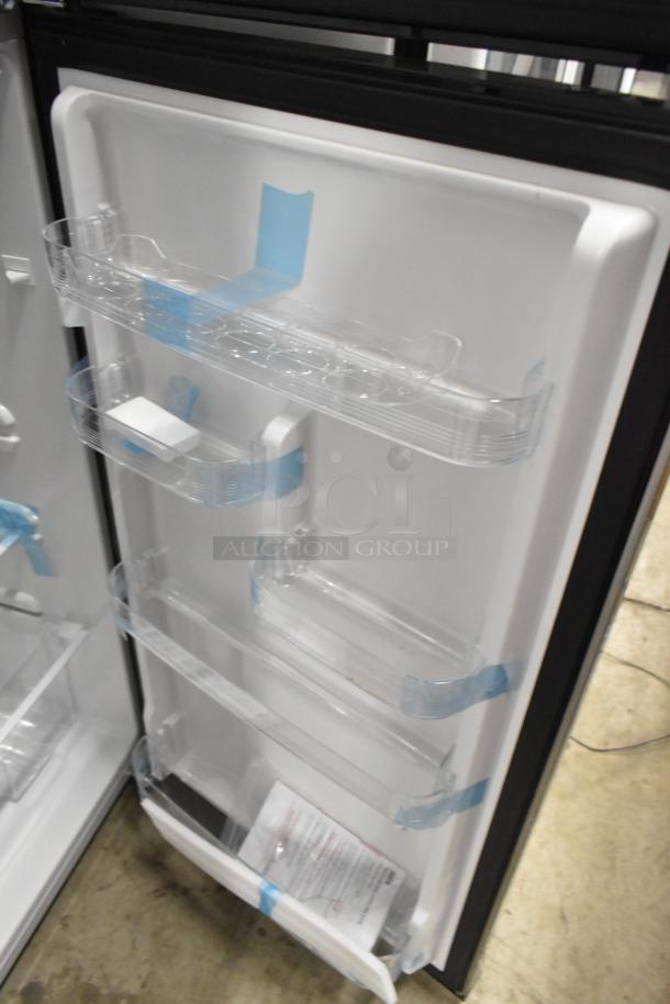 Frigidaire FGFR727 metal reach-in cooler with freezer, pristine condition, 115 volts, 1 phase. Blue tape remnants on shelves.