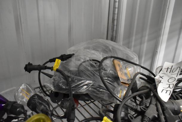 Bundle of five string lights with black cords and yellow tags on a metal shelf. Some bulbs are visible. Wrapped in plastic, good condition.