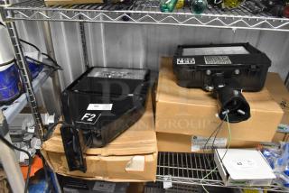 Four black flood lights on shelves with tags. Includes labels "F2" and "62 LED." Appears unused, in excellent condition.