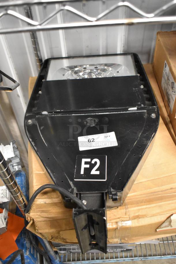 Black flood light with metal housing, labeled "F2" and marked "62." Light sits on a shelf; visible wear on edges.