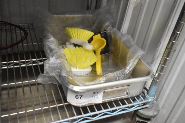 4 brand new items: Yellow handheld lemon juicer, two cleaning brushes, in an aluminum roasting pan with handles. Labels visible.
