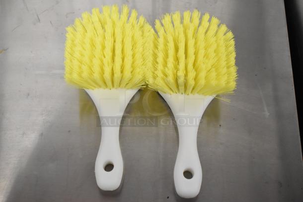Two new yellow handheld brushes with white handles, ideal for cleaning, shown on a metal surface.