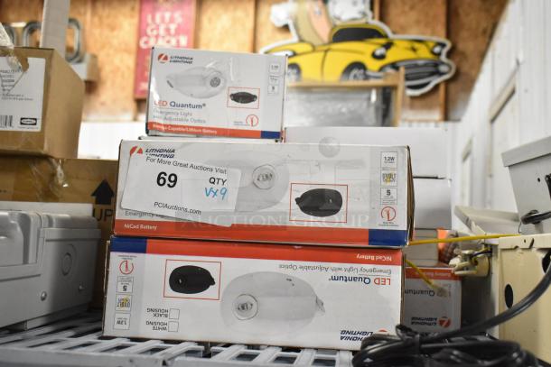 Stack of Lithonia Lighting emergency lights and exit signs in boxes, labeled "LED Quantum." Auction tag shows quantity "9."