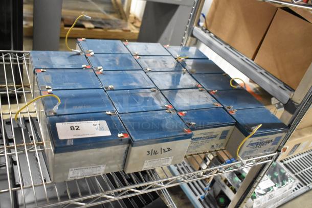 19 Power Sonic PS-1276 rechargeable batteries on metal shelf, each with blue casing, labeled with quantity and date.