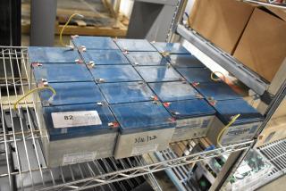 19 Power Sonic PS-1276 rechargeable batteries on metal shelf, each with blue casing, labeled with quantity and date.