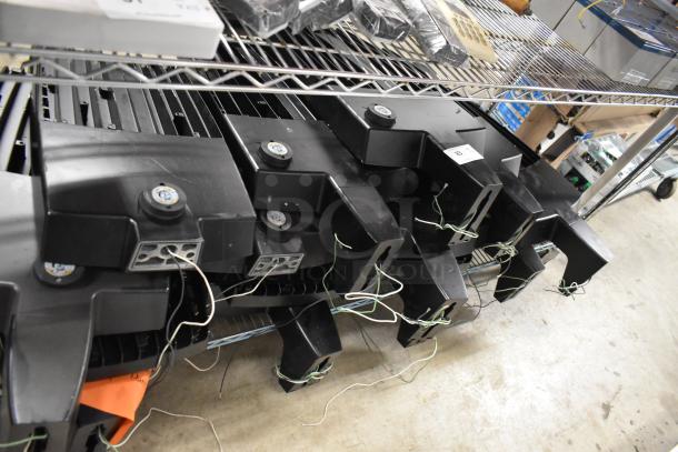 Stack of 16 black flood lights with wiring on metal shelf, ready for auction. Multiple units increase bid value.