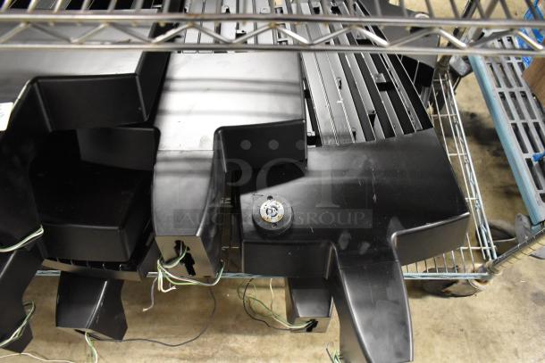 16 black flood light housings on metal racks, featuring wiring and connectors, in used condition.