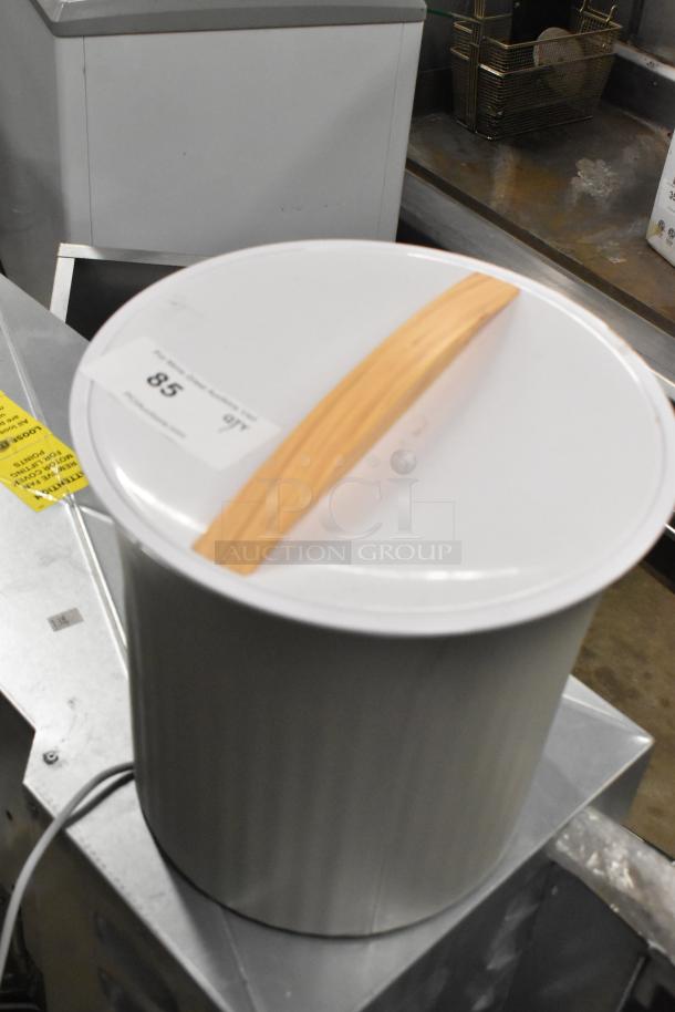 Towel warmer with wooden handle, 115 volts, 1 phase, in good condition. Features a metal body with a white lid.