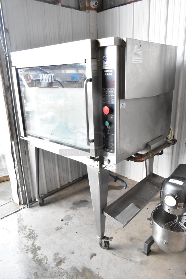 Hardt Inferno 3500 stainless steel commercial rotisserie oven, natural gas, with skewers and metal legs on casters, in good condition.