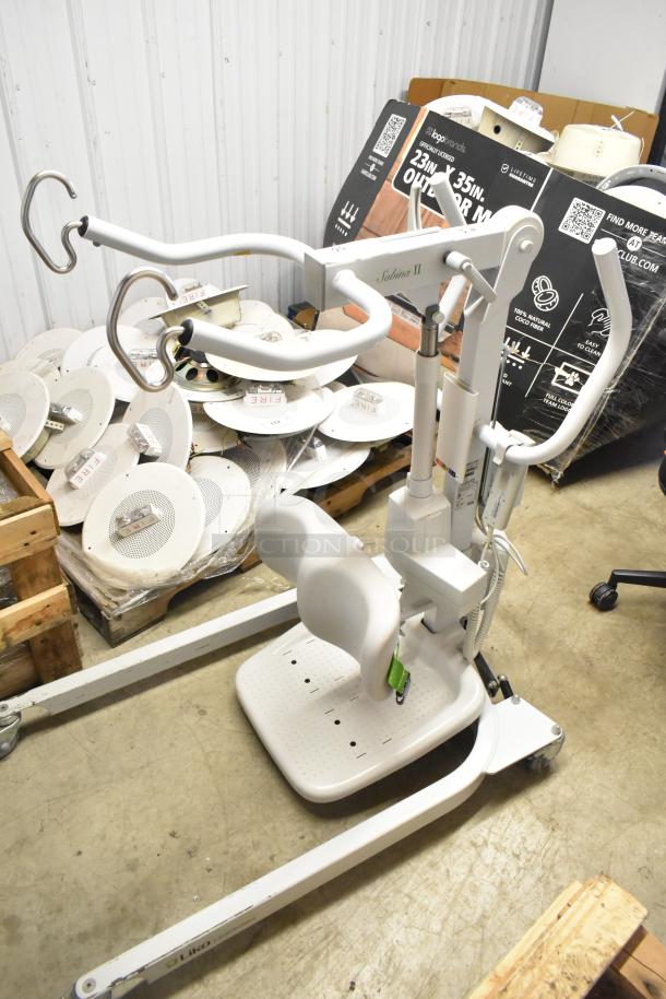 Sabina II Sit To Stand Patient Lift, white, features ergonomic design, adjustable arm, and sturdy base, minor wear visible.