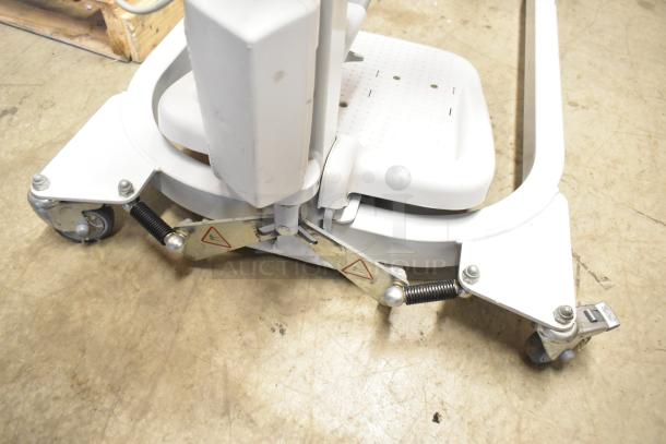 Sabina II Sit To Stand Patient Lift, white, sturdy base with casters, in used condition.