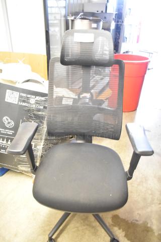 Black mesh office chair on casters featuring adjustable armrests and headrest, in good condition.