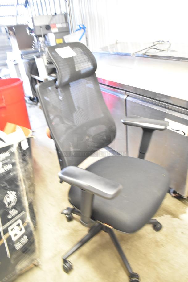 Black office chair on casters with adjustable armrests and mesh back. Gently used condition. Features label on back.
