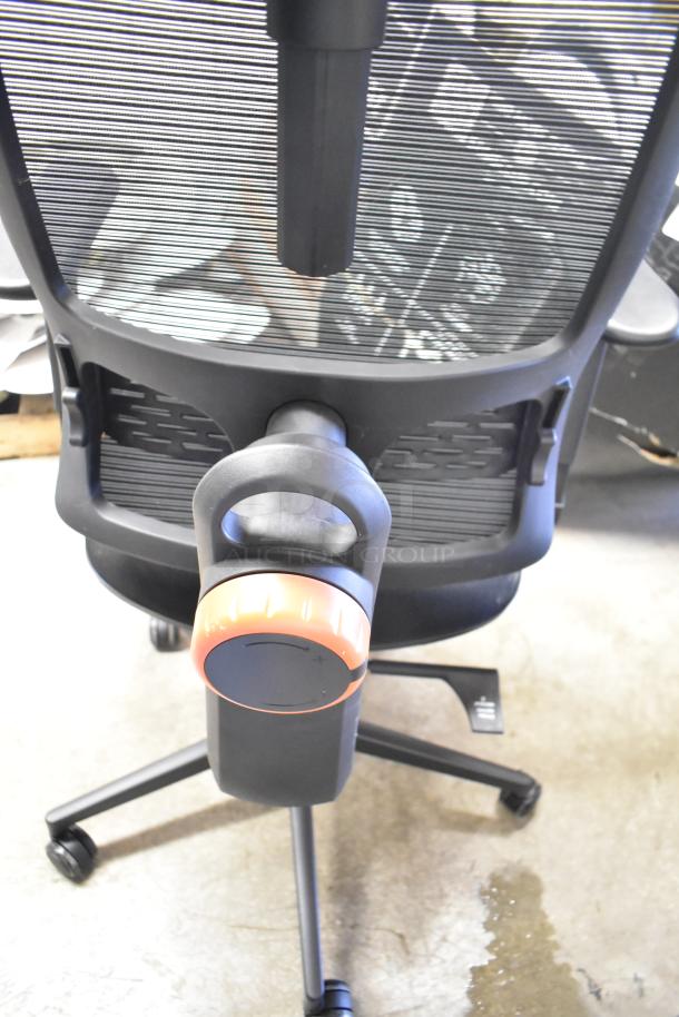 Black office chair with mesh back, adjustable armrest, black casters, and an orange tension knob, in excellent condition.