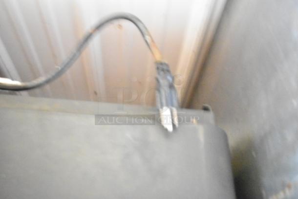 Blurry image of a power cord and a section of a metal appliance. Unable to discern specific details or markings.