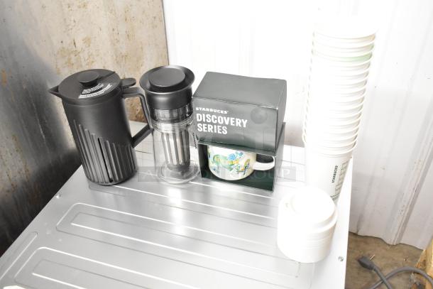 Lot of items including Starbucks Discovery Series mug, black carafe, clear infuser, and stack of white cups.