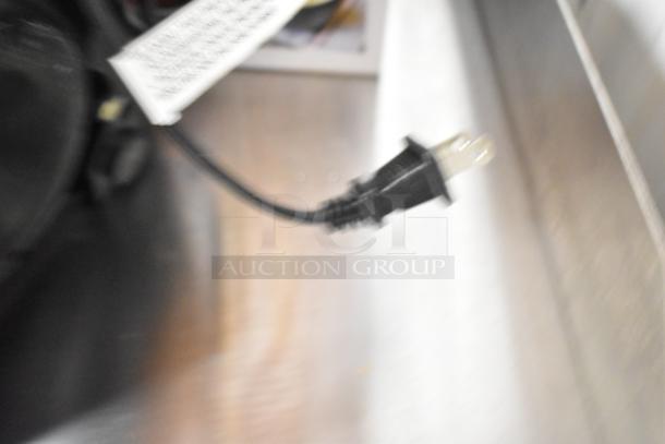 Blurred image of a Ninja countertop food blender plug. Black cord with a visible two-prong plug. No visible blender or pitcher.