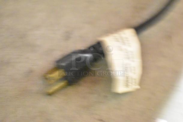 Blurry image of an electrical plug with a label. No visible machine or detailed features are discernible.