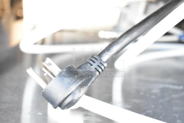 Close-up of a power plug for a 2024 Follett HMC1410WBT nugget ice machine, showing its metal prongs and black cord.