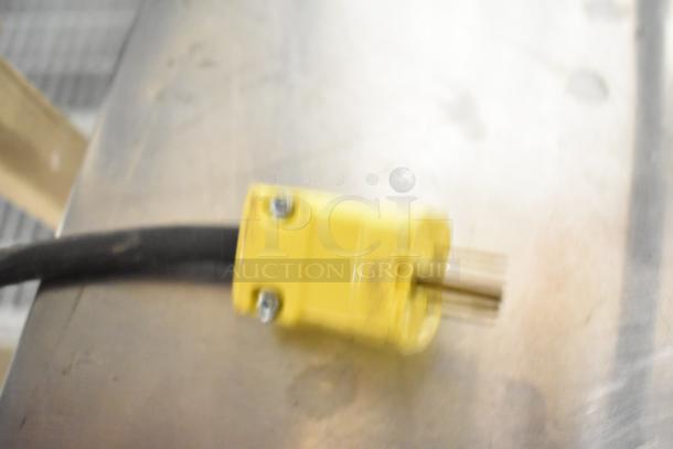 Blurry image showing a yellow electrical plug for a Pavoni New CookMatic tartlet machine, highlighting its 110V connection.
