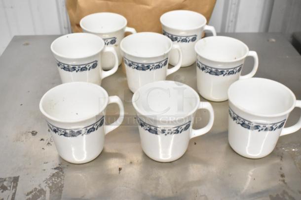 Eight white ceramic mugs with a blue floral band, gently used condition, ideal for kitchen use.